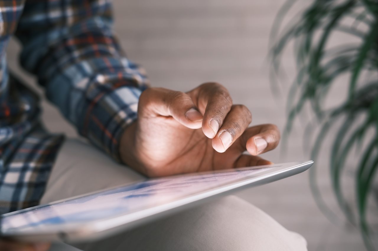 A man's arm in a plaid shirt sleeve hovers over a glowing digital tablet screen