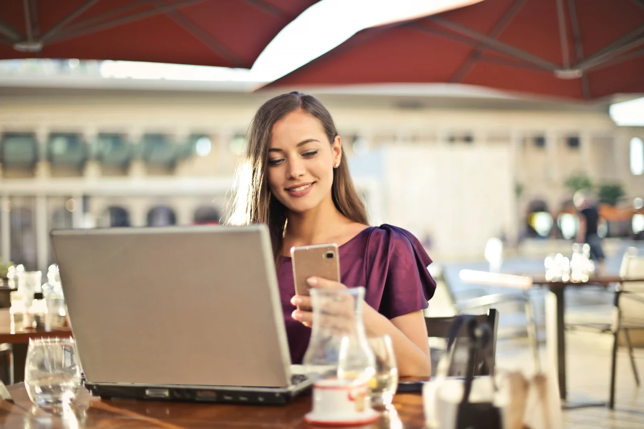 woman at computer screen and mobile phone wearing purple top
